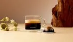 Чашка кофе Nespresso на столе с капсулой.